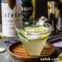 The Purring Blur 7 The Tipsy Cat cocktail in a martini glass, garnished with cucumber and lemon.