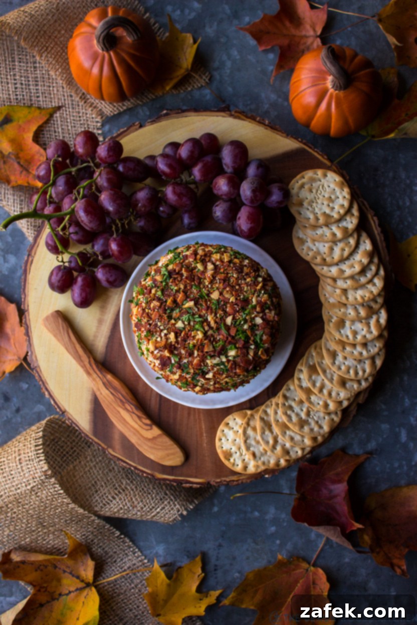 Overhead shot of a beautifully presented Jalapeño Bacon Ranch Cheese Ball on a rustic wooden platter, artfully arranged with various crackers and clusters of fresh green grapes.