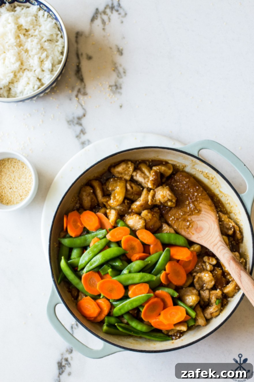 Effortless Sticky Sesame Chicken 4 Close-up overhead shot of Easy Sesame Chicken, glistening with sauce, alongside bright carrots and sugar snap peas.