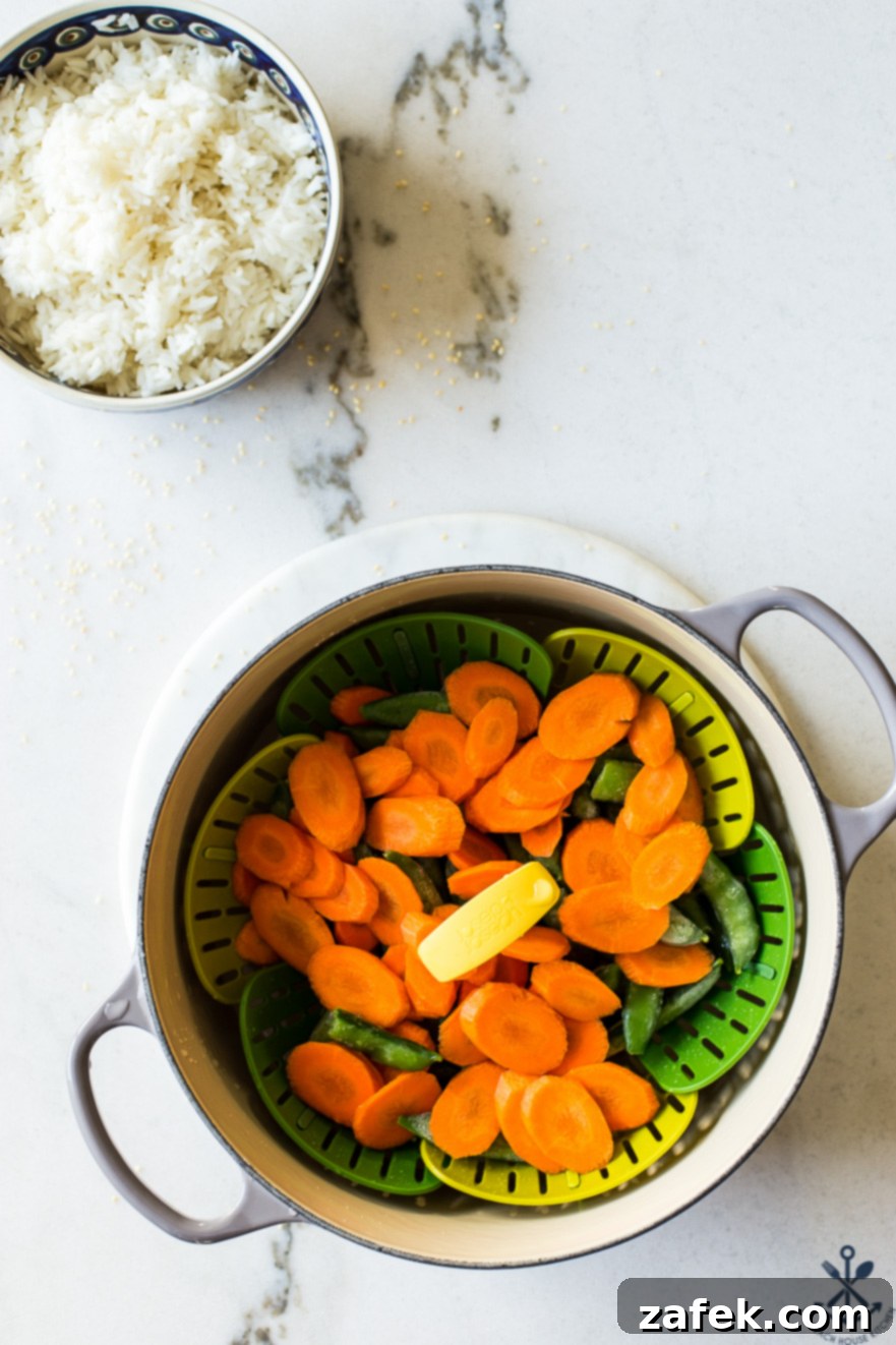 Effortless Sticky Sesame Chicken 7 Steamed carrots and sugar snap peas in a pot with a bowl of fluffy white rice, ready to accompany the sesame chicken.