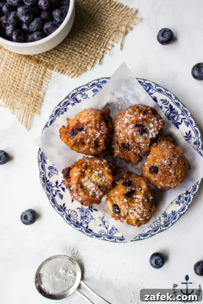 Golden brown blueberry fritters dusted with powdered sugar, served on a white plate