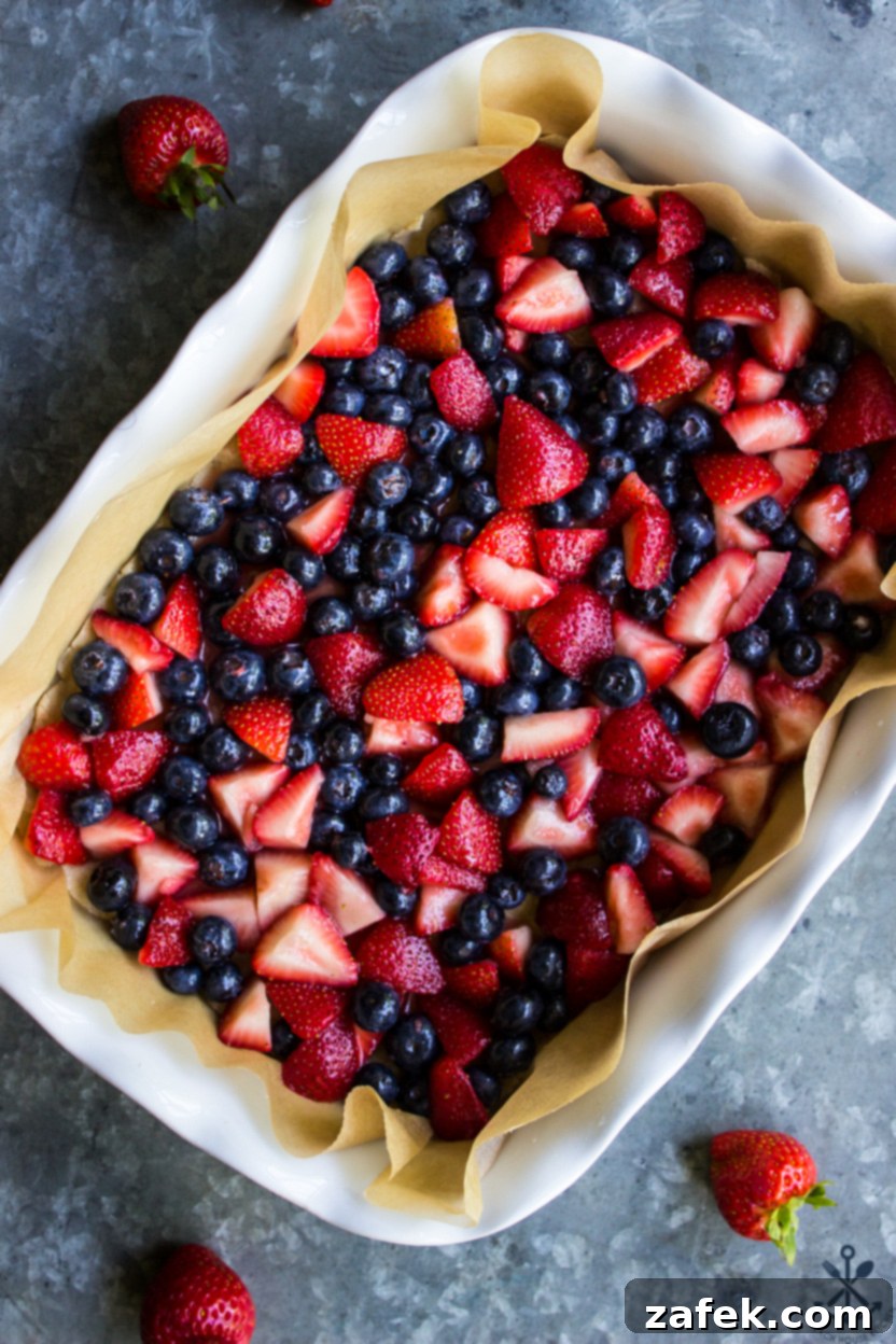 Summer Berry Streusel Bars 4 Overhead photo of a baking dish of unbaked berry bars topped with fresh strawberries and blueberries before the crumb topping is added.