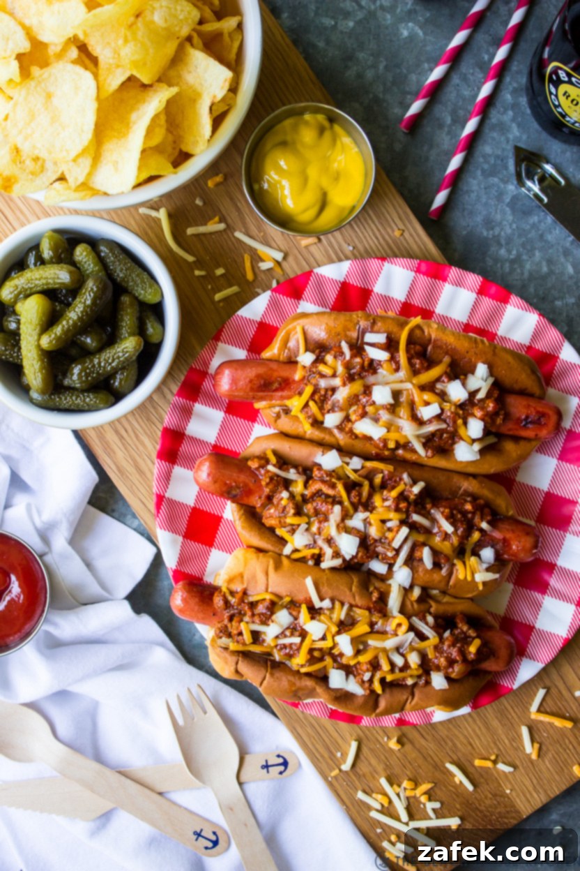 Overhead photo of a plate of chili dogs surrounded by a bowl of pickles, chips and a small bowl of mustard