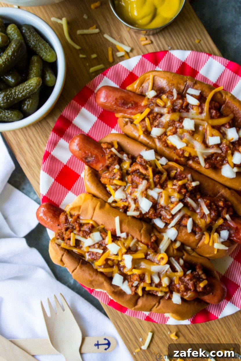 Up close overhead photo of a plate f chili dogs topped with chopped onions and shredded cheese