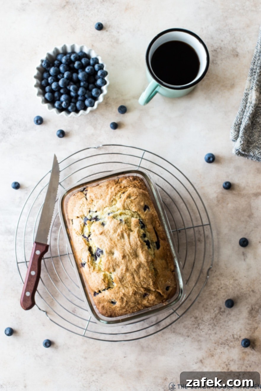 Blueberry Lemon Loaf 5 Blueberry lemon loaf on a round wire rack with a bowl of blueberries and a cup of coffee next to the rack