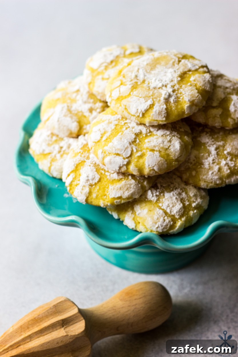 A small cake stand topped with multiple lemon crinkle cookies, showing their distinct powdered sugar coating and cracks