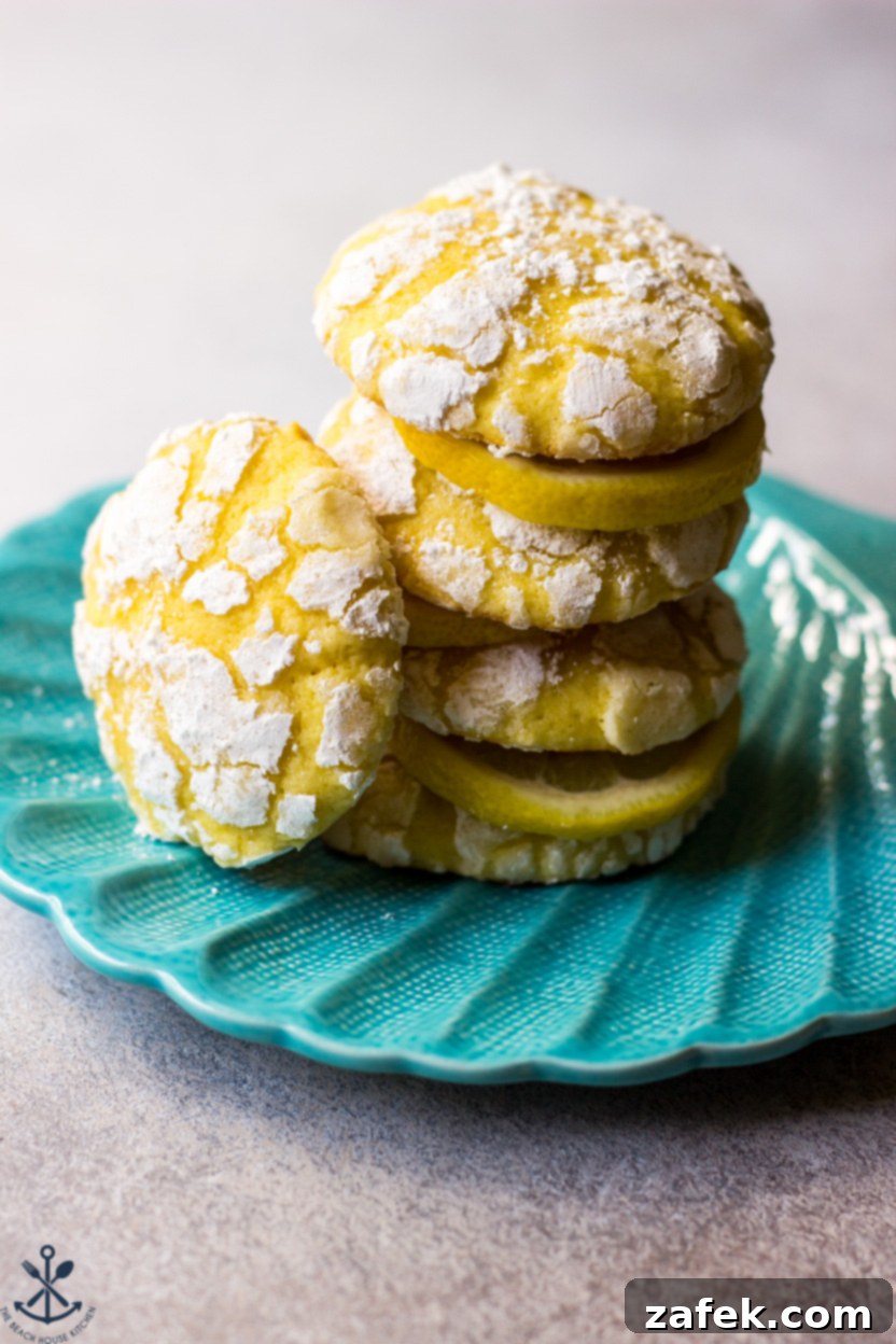 A stack of golden lemon cookies dusted with powdered sugar, resting on a turquoise shell plate
