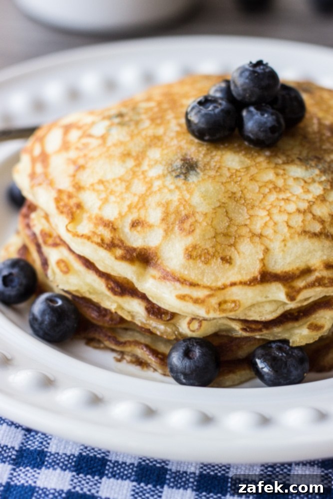 Fluffy Buttermilk Blueberry Stacks 4 Buttermilk blueberry pancake batter being poured onto a hot griddle, with blueberries just added, ready to cook to golden perfection.