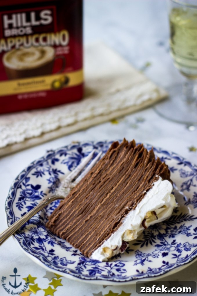 Double-Chocolate-Hazelnut-Crepe Cake A perfectly cut slice of Double Chocolate Hazelnut Crepe Cake rests on a charming blue and white patterned plate, with a coffee container softly blurred in the background, inviting a moment of indulgence.