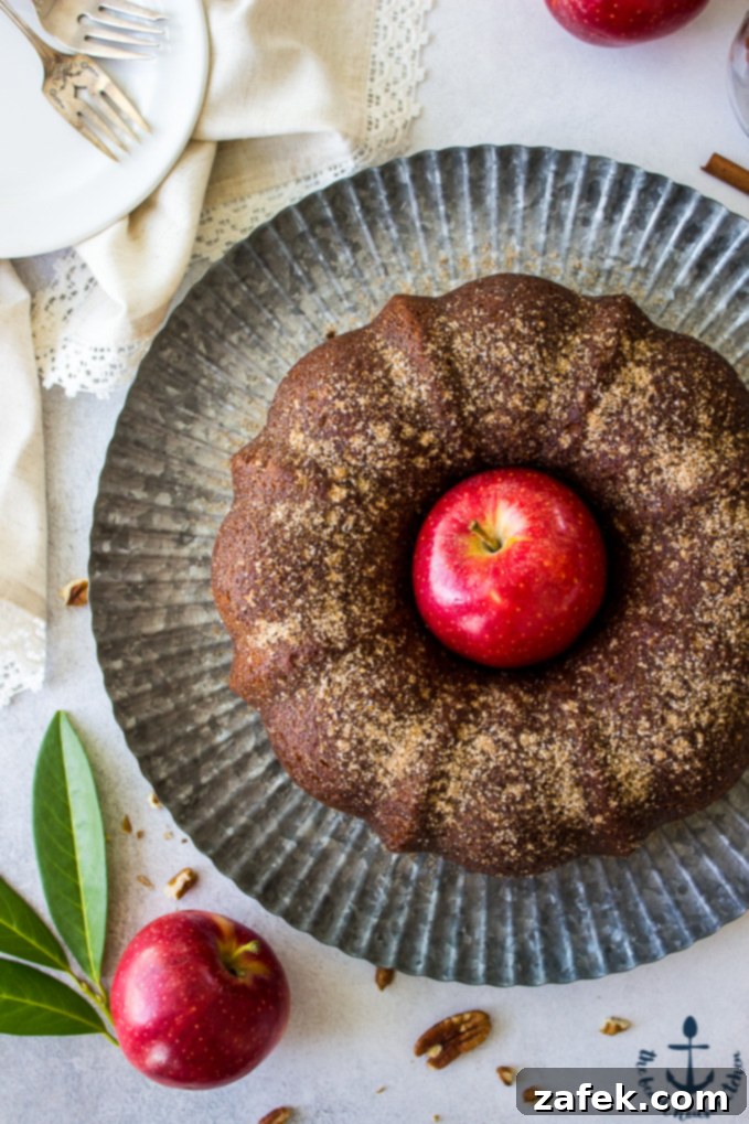 Overhead photo of Apple Cider Doughnut Bundt Cake with Pecan Brown Sugar Ripple with a red apple in the middle of cake on a silver tray.