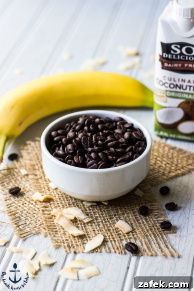 Espresso-Beans-and-Banana A small white bowl brimming with dark espresso beans, positioned in front of a ripe yellow banana, suggesting key ingredients for a coffee-infused treat.