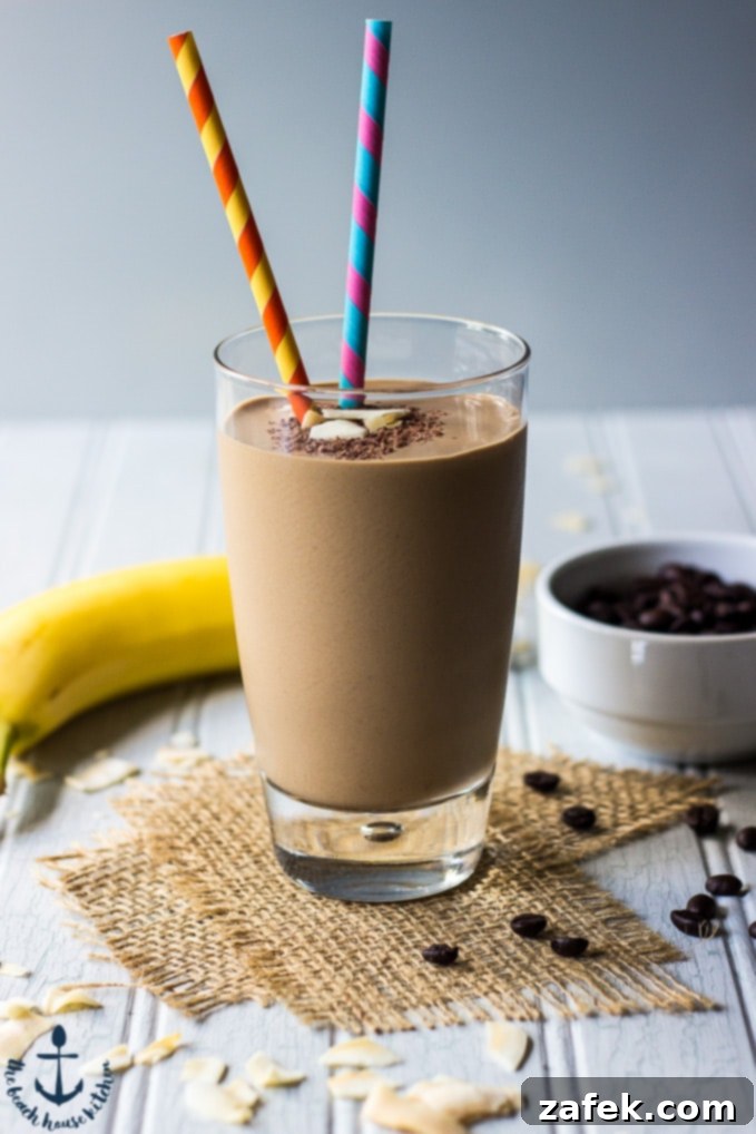 Chocolate-Coconut-Coffee-Smoothie A close-up shot of a creamy chocolate coconut espresso smoothie in a clear glass, adorned with chocolate shavings and toasted coconut chips, featuring two vibrant straws, on a rustic burlap ribbon.