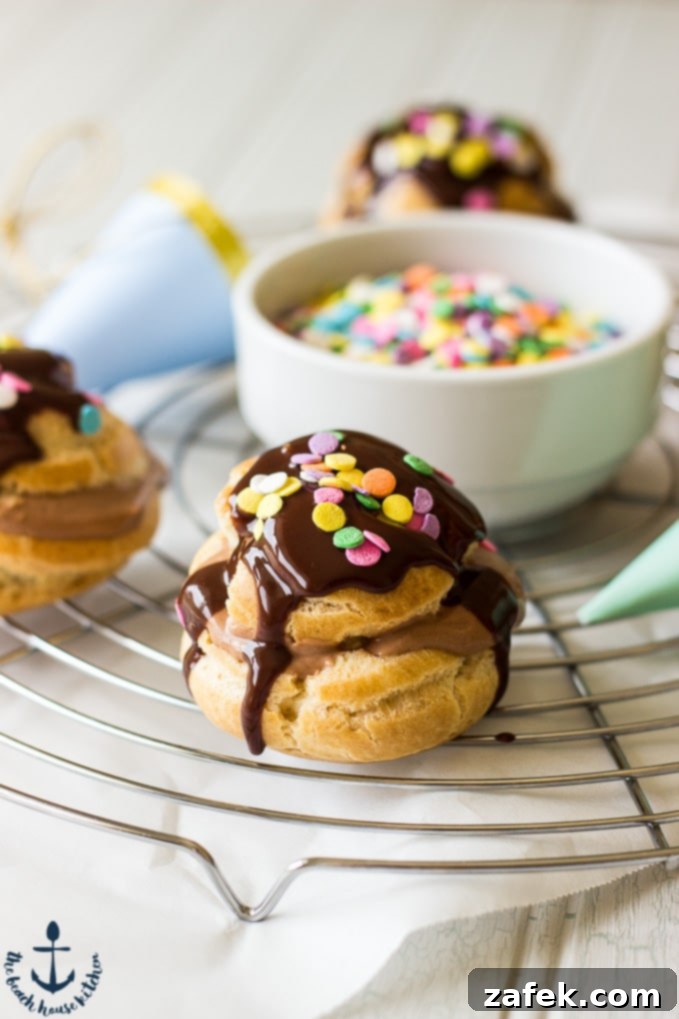 Nutella-Cream-Puffs Nutella Cream Puffs drizzled with chocolate and sprinkles on a round silver cooling rack with a white bowl of sprinkles in in center of rack.