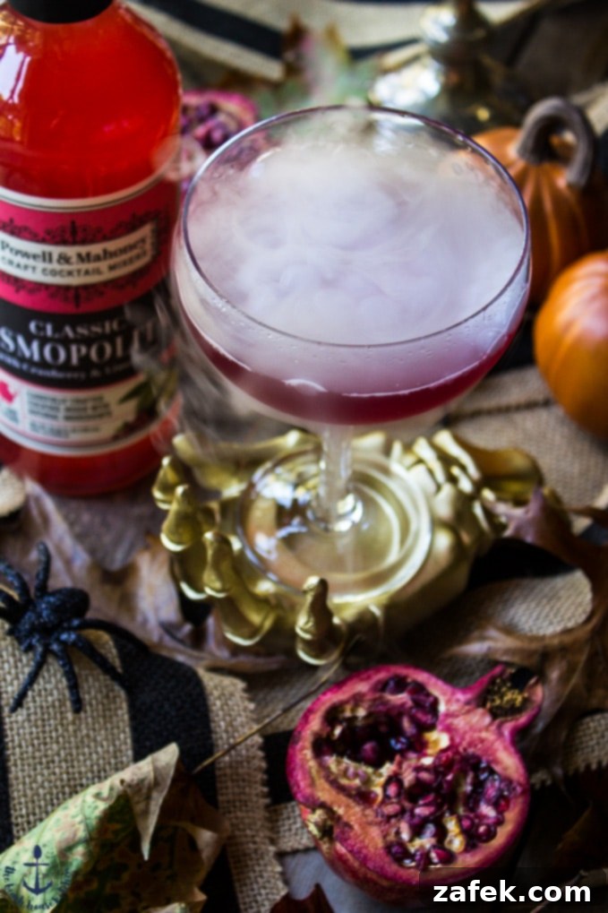 Vampires-Venom-Cocktail The Vampire's Venom Cocktail with dry ice bubbling in a gold skeleton hand with cocktail mixer bottle and half a pomegranate.