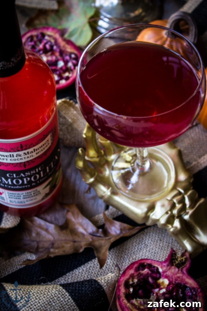 Vampires-Venom-Cocktail The Vampire's Venom Cocktail in a gold skeleton hand with a red bottle of cocktail mixer and a half a pomegranate.