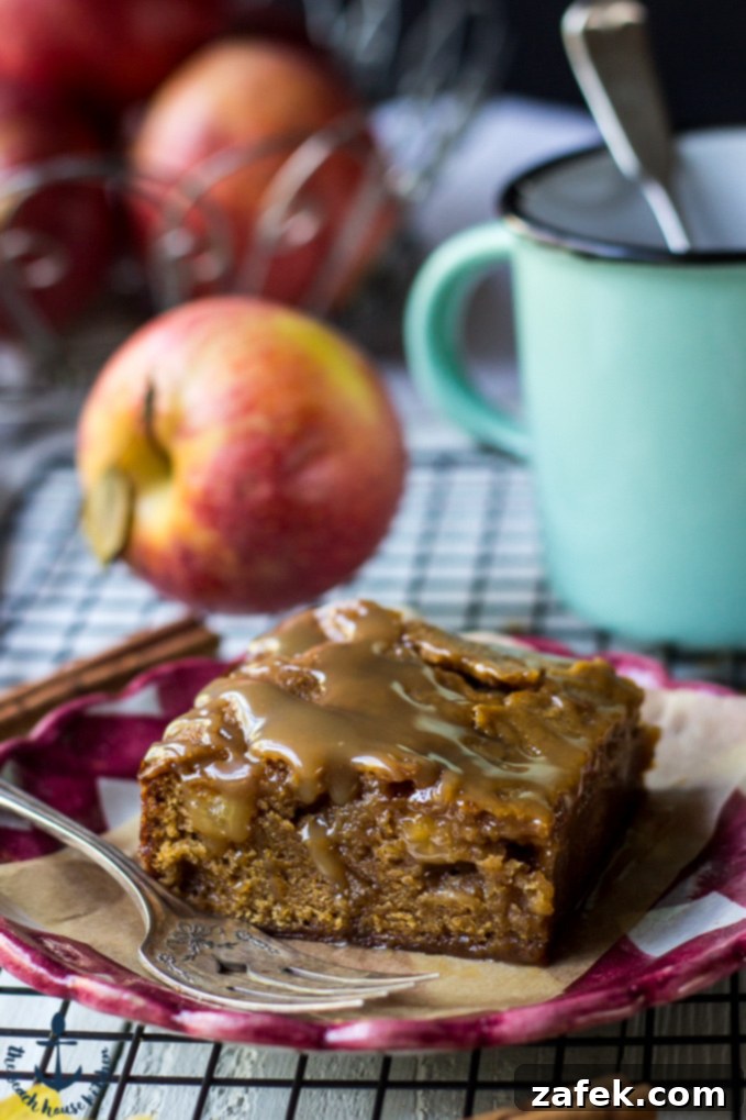 A single Caramel Glazed Apple Butter Blondie on a charming red and white check plate, with a fresh red apple and a green mug blurred in the background, hinting at cozy fall vibes.