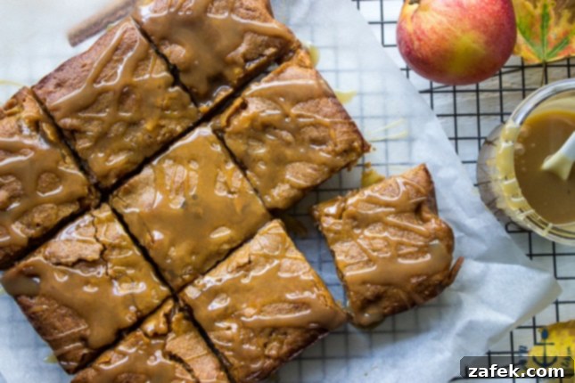 An overhead view of freshly baked Caramel Glazed Apple Butter Blondies, cooling on white parchment paper over a wire rack, glistening with caramel drizzle.