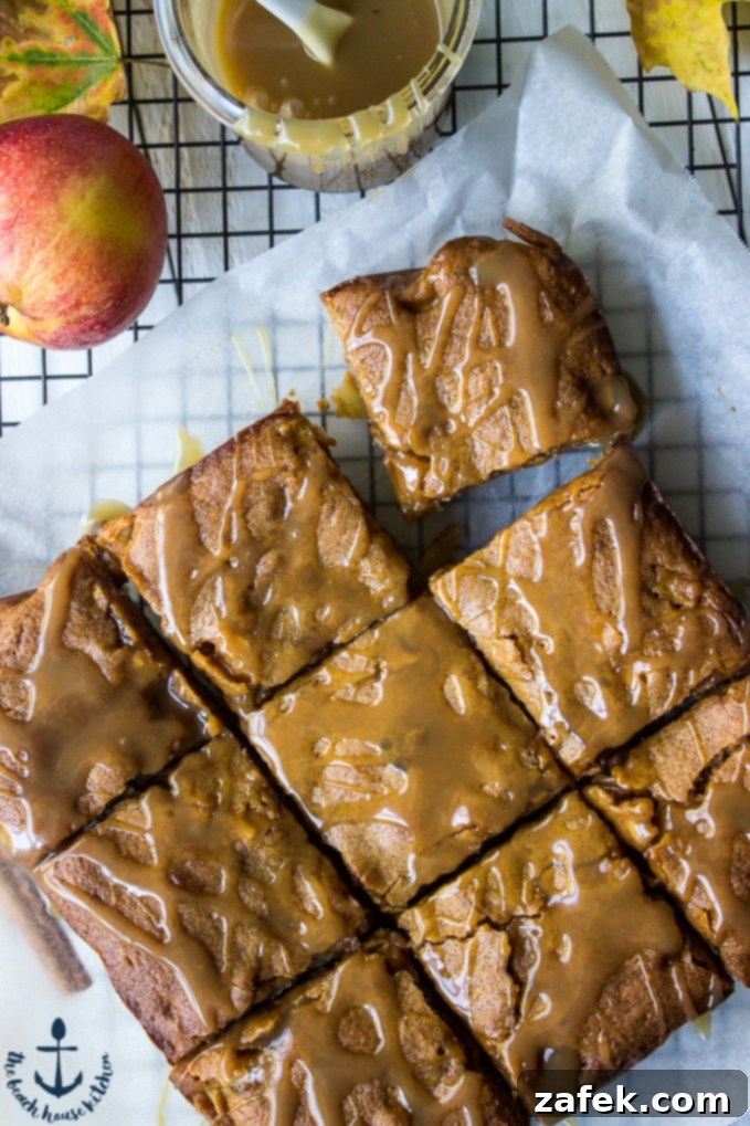 An inviting overhead photo of an entire pan of Caramel Glazed Apple Butter Blondies, glistening with a generous caramel drizzle, cooling on white parchment paper over a wire rack, ready to be sliced.