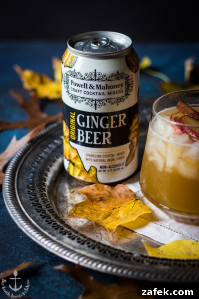 Dark-Stormy-Cocktail A can of Powell & Mahoney Ginger Beer resting on a silver tray beside a Fall Dark 'N' Stormy cocktail, adorned with a single autumn leaf.