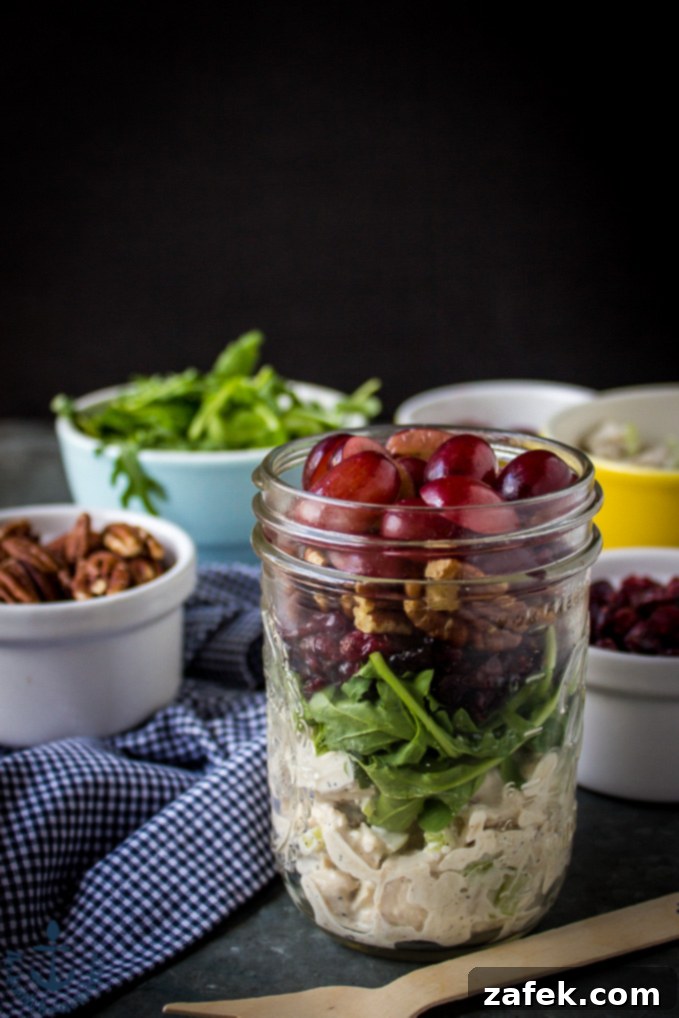 Turkey Salad with Grapes, Pecans and Cranberries in a Jar served with fresh arugula and a scattering of pecans, against a backdrop of a blue and white checked napkin.