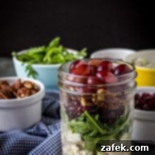 A circular image featuring the prepared Turkey Salad with Grapes, Pecans and Cranberries in a Jar, with pecans and arugula visible in white bowls, alongside a blue and white checked napkin.