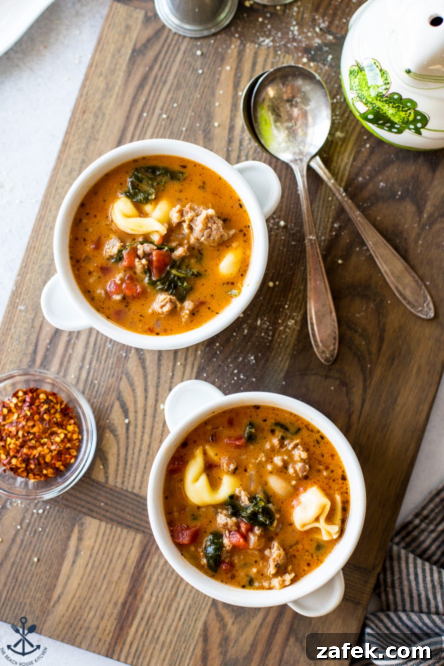 Overhead photo of two white bowls on a wooden board filled with tomato tortellini stew, adorned with a sprig of fresh basil.
