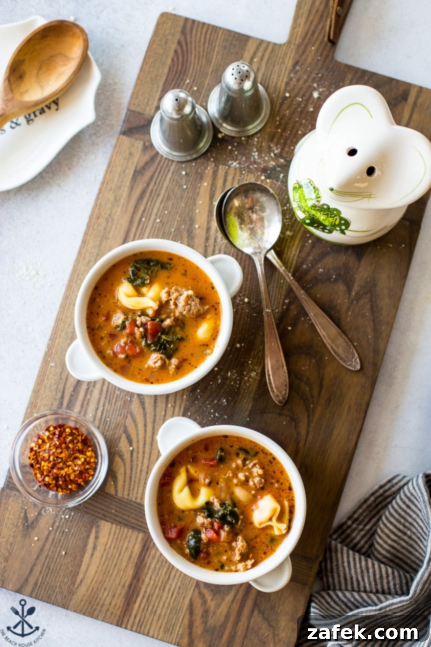 Two bowls filled with vibrant tomato tortellini stew on a rustic wooden board, accompanied by two metal spoons.