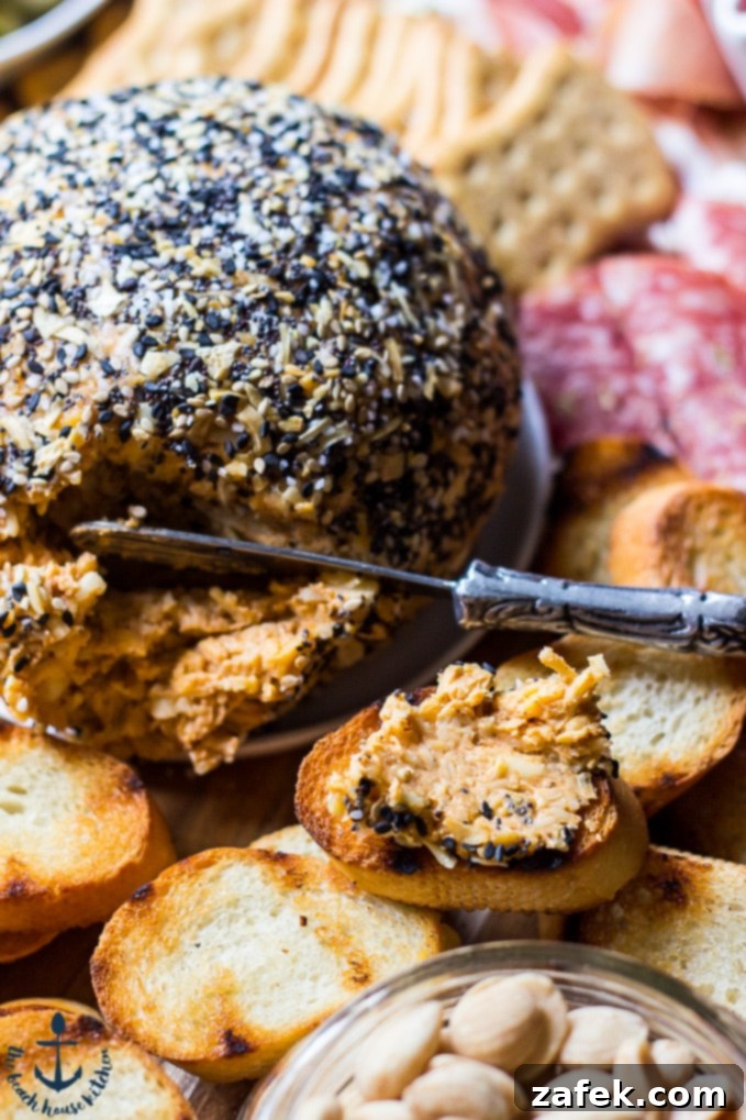 Epic Fall Cheese Board - Everything Cheddar Horseradish Cheese Ball Close-up shot of the textured Everything Cheddar Horseradish Cheese Ball, accompanied by a small serving knife and an array of crispy crackers, inviting a taste.