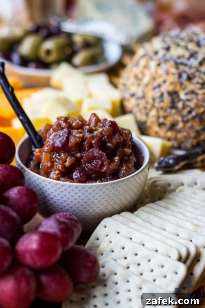 Epic Fall Cheese Board - Everything Cheddar Horseradish Cheese Ball Detailed close-up of a white polka dot bowl filled with vibrant chutney, artfully surrounded by an assortment of crackers, fresh grapes, black olives, and various gourmet cheeses on a large cheese board.