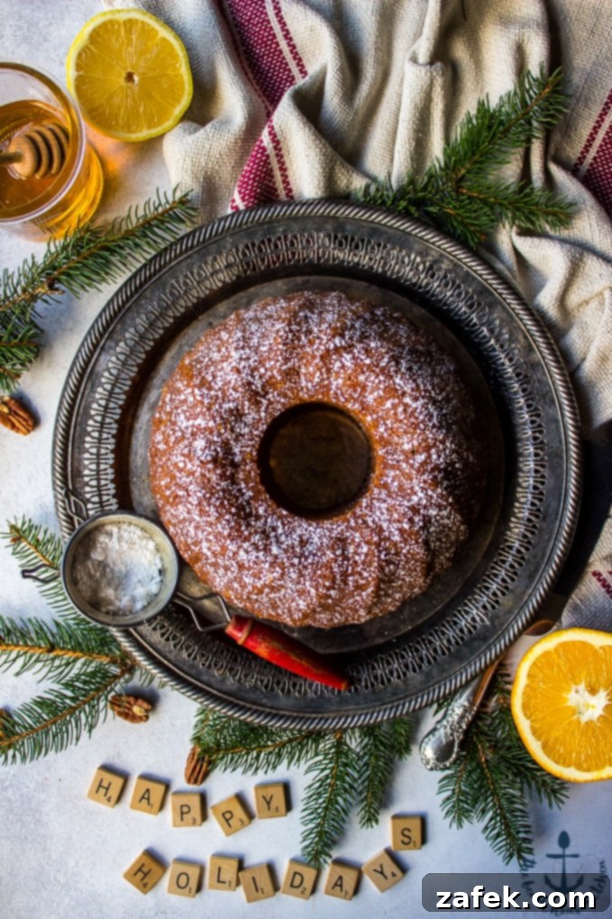 Honey-Pecan-Bundt-Cake Overhead photo of Honey Pecan Bundt Cake on silver tray with greens, scrabble tiles spelling Happy Holidays, cake knife, sifter, honey and lemon in background.