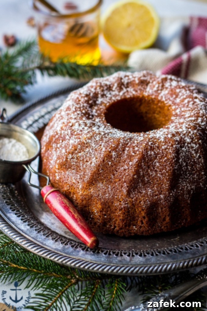 Honey-Pecan-Bundt-Cake Honey Pecan Bundt Cake on silver tray with greens, cake knife, sifter, honey and lemon in background.
