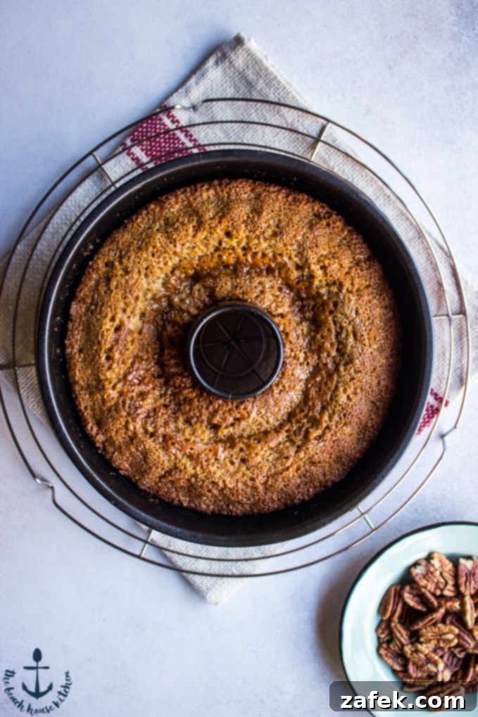 Honey-Pecan-Bundt-Cake Overhead photo of Honey Pecan Bundt Cake fresh out of oven on wire rack with pecan on small green plate.