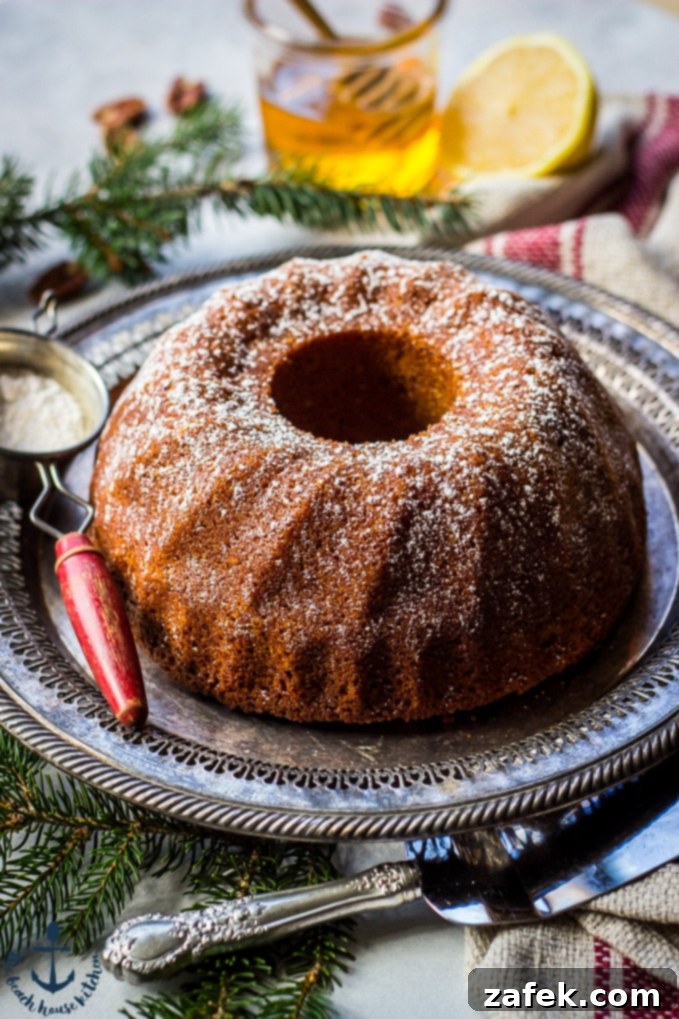 Honey-Pecan-Bundt-Cake Honey Pecan Bundt Cake on silver tray with greens, cake knife, sifter, honey and lemon in background.