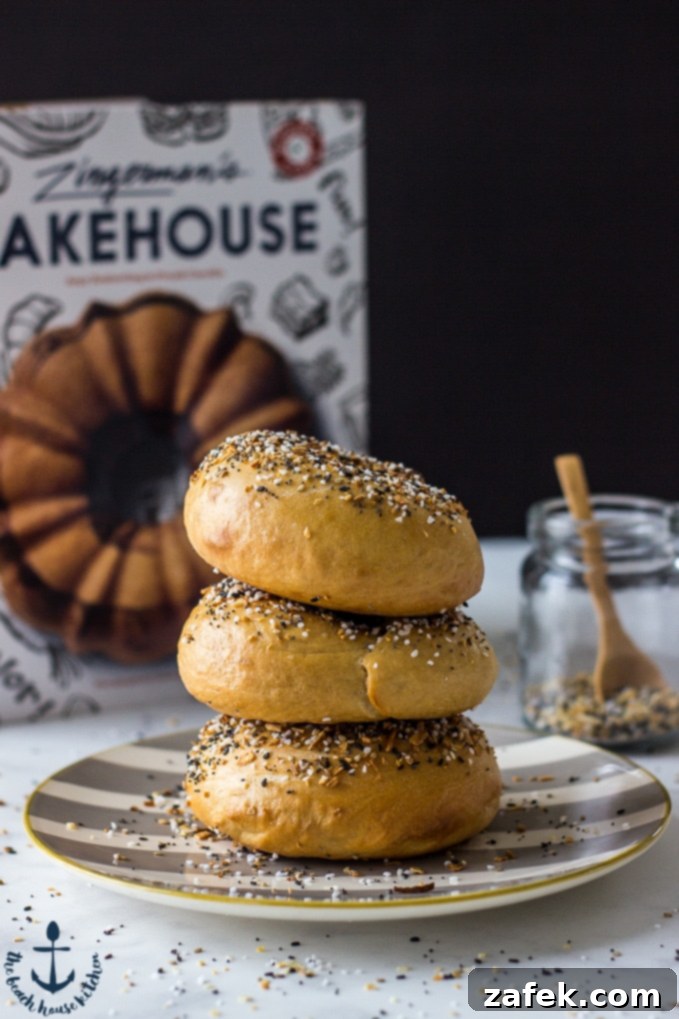 Zingerman's Bakehouse Cookbook A stack of three Everything Bagels on a striped plate, with a Zingerman's cookbook and a jar of everything bagel seasoning in the background.