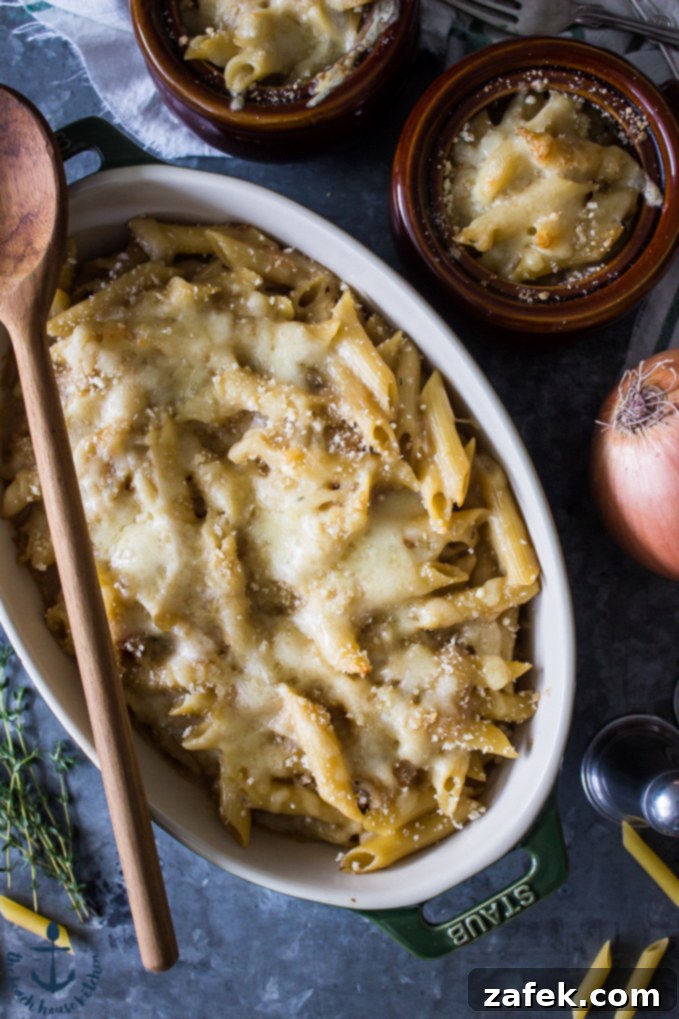 Creamy French Onion Pasta with Melted Cheese Close-up overhead view of the French onion pasta bake in a baking dish, showcasing the golden-brown crust, bubbly cheese, and the texture of the penne pasta intertwined with caramelized onions. Smaller serving bowls hint at the delightful individual portions.