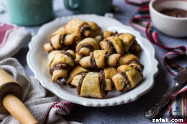 Nutella-Pecan-Rugelach Nutella Pecan Rugelach on white platter with cup of cocoa with marshmallows in mug, bowl of melted Nutella and rolling pin.