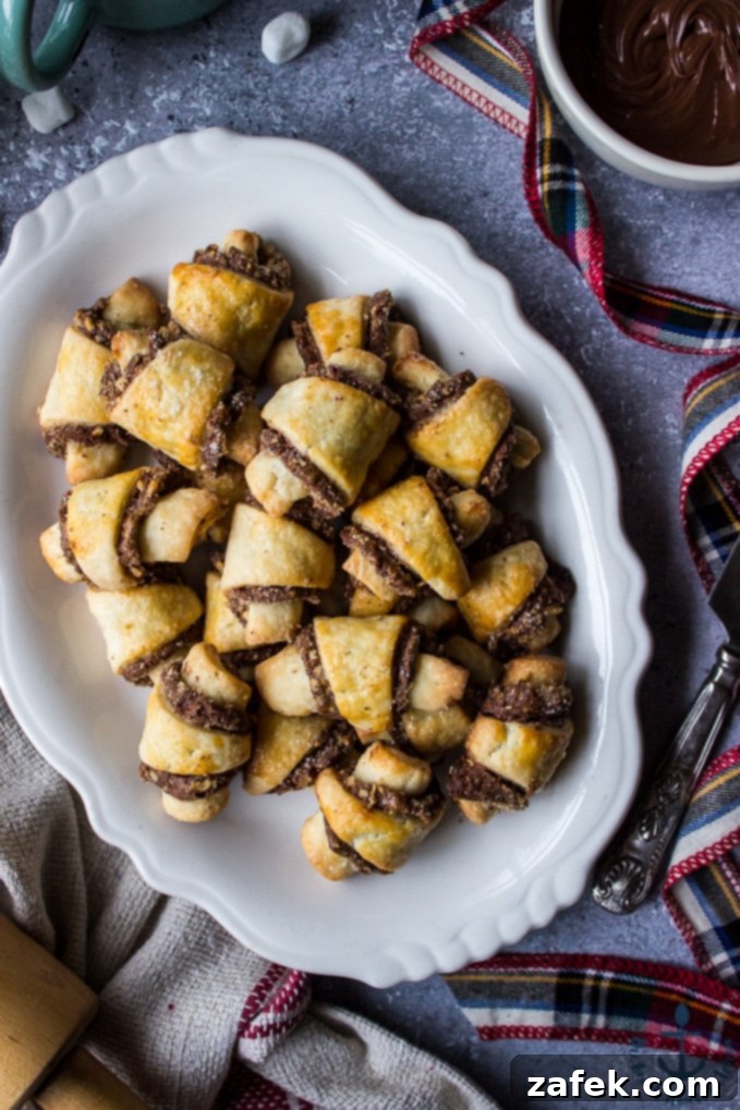 Nutella-Pecan-Rugelach Nutella Pecan Rugelach on white platter with bowl of melted Nutella, rolling pin and plaid ribbon.