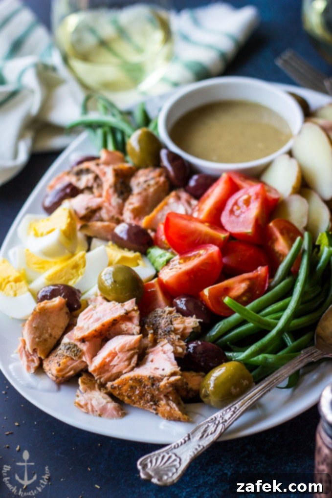 Close-up shot of Salmon Nicoise Salad with Dijon Vinaigrette on white platter with a silver spoon, showcasing the rich texture of the salmon and fresh vegetables.