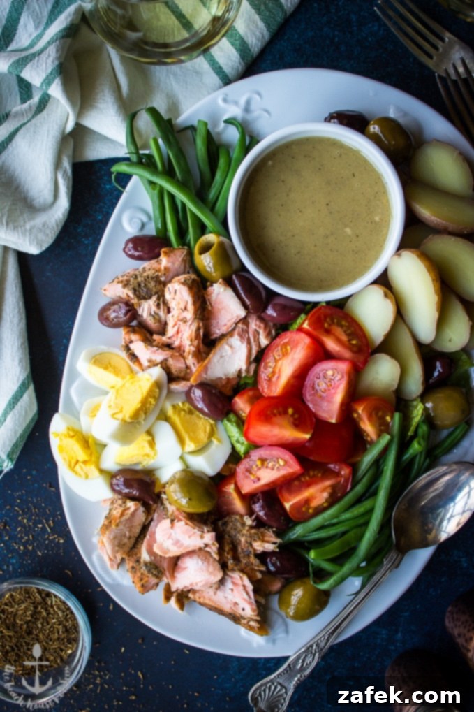 Overhead shot of Salmon Nicoise Salad with Dijon Vinaigrette on white platter, displaying the artful arrangement of each ingredient for a visually appealing dish.