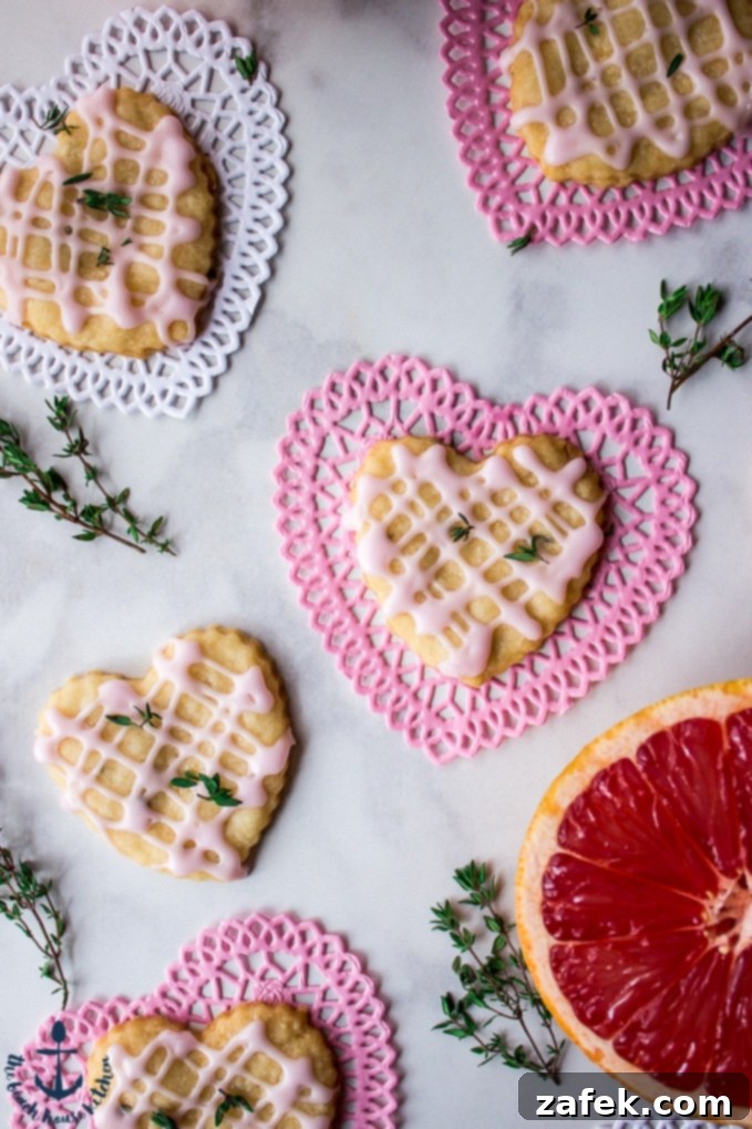 Beautifully arranged Pink Grapefruit and Thyme Shortbread Heart cookies on elegant pink and white Valentine heart doilies, garnished with fresh sprigs of thyme and slices of pink grapefruit, capturing the essence of romance and fresh flavors.