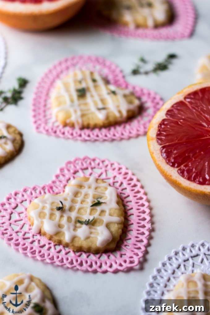 Artfully arranged Pink Grapefruit and Thyme Shortbread Heart cookies displayed on charming heart-shaped doilies, with fresh pink grapefruits and fragrant thyme springs subtly blurred in the background, highlighting the key ingredients.