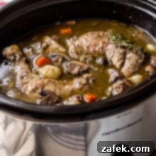 Effortless Slow Cooker Coq Au Vin 2 Coq Au Vin in a silver slow cooker with a bottle of wine and salt and pepper shakers in background.