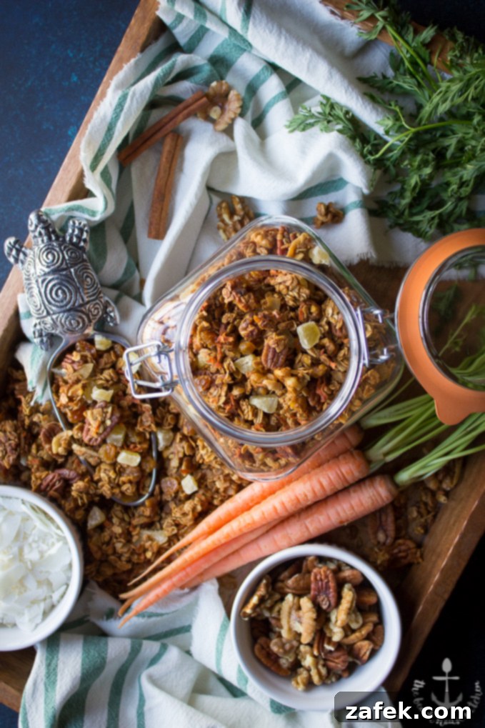 Carrot-Cake-Granola Overhead shot of carrot cake granola in jar on tray with bowls of nuts and coconut, carrots, and scooper filled with granola.