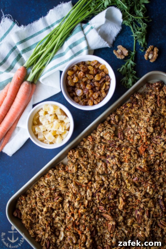 Carrot-Cake Granola Overhead shot of baked carrot cake granola on baking sheet with dried pineapple and golden raisins in bowls and bunch of carrots on the side.