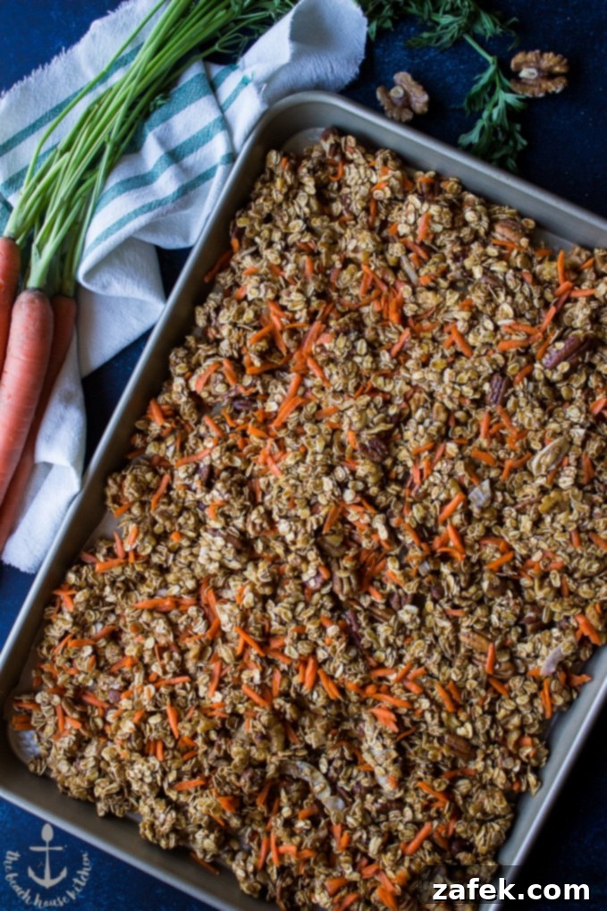 Carrot-Cake-Granola Overhead shot of pre-baked carrot cake granola on baking sheet with bunch of carrots.