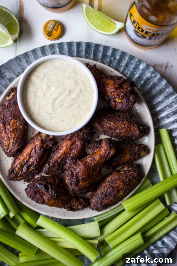 Baked-Spicy-Dry-Rub-Wings-White-BBQ-Sauce Overhead shot of spicy baked spicy wings with white bbq sauce on tray with celery and beer and lime in background.