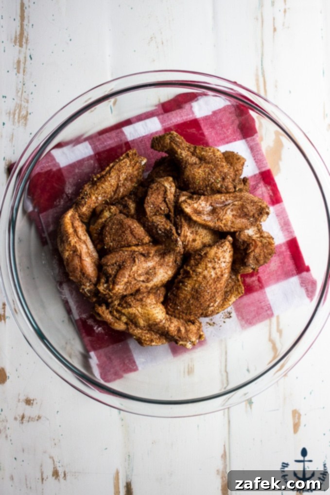 Baked-Spicy-Dry-Rub-Wings-White-BBQ-Sauce Overhead shot of wings coated in spicy rub in glass bowl on red and white checked napkin.