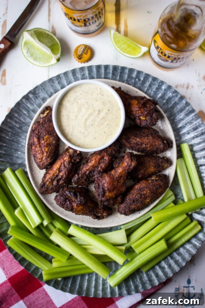 Baked-Spicy-Dry-Rub-Wings-White-BBQ-Sauce Overhead shot of spicy baked spicy wings with white bbq sauce on tray with celery and beer and lime in background.