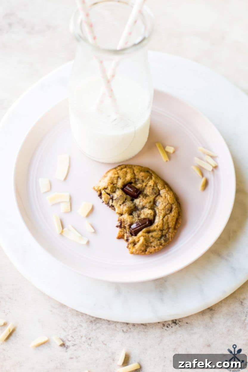 Coconut Almond Chocolate Chip Bliss Cookies 3 A half of a chocolate chip cookie on a pale pink plate with a bottle of milk