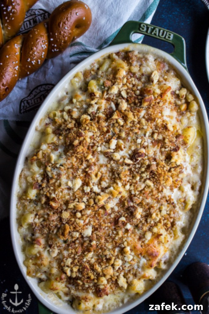 A top-down view of creamy Philly Cheesesteak Macaroni and Cheese in an oval baking dish, with two soft pretzels in the background, hinting at its Philadelphia origins.